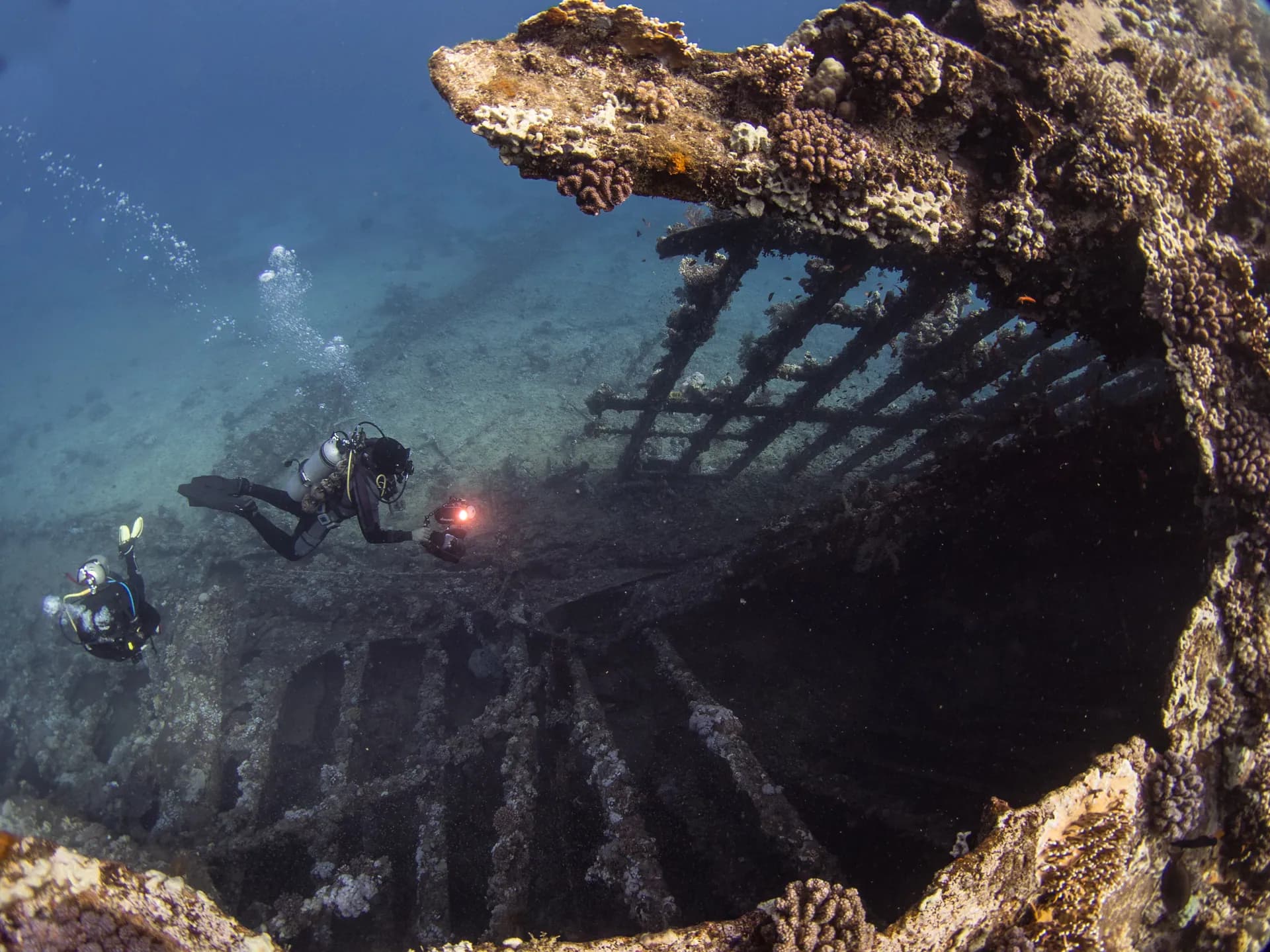 Scuba divers exploring the broken hull of the Hamada wreck at Abu Ghusun, Red Sea